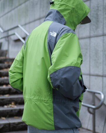 ゴールドウインオンラインストア公式 | STAFF PICKS AUTUMN OUTERWEAR STYLE | ライムグリーン×グレーの防水シェルジャケットのバックスタイル。肩から袖にかけた切り替えデザインとフード形状がわかる後ろ姿。