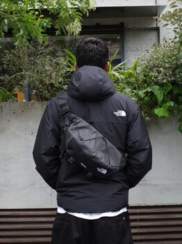 ゴールドウインオンラインストア公式 | STAFF PICKS AUTUMN OUTERWEAR STYLE | ブラックカラーのフード付きシェルジャケットを着用し、同系色のスリングバッグを合わせた都市型アウトドアスタイルのバックルック。