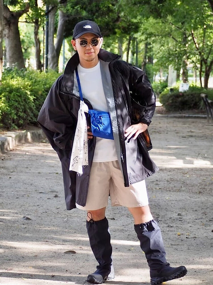 ゴールドウインオンラインストア公式 | STAFF STYLE | ブラックの防水レインポンチョにショートパンツとロングゲイターを合わせ、フェスや雨天のアウトドアに適したスタイルを着用したモデルの全身ルック