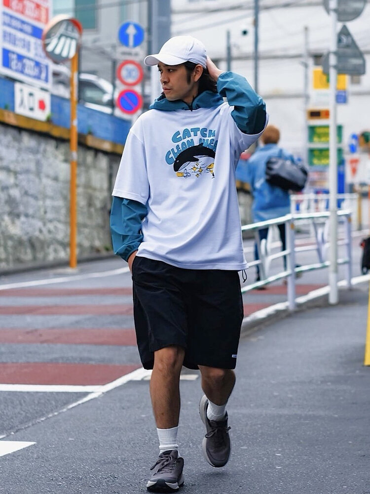 ゴールドウインオンラインストア公式 | STAFF STYLE | グラフィックTシャツにウィンドシェルをインナーとしてレイヤード。ショートパンツを合わせたカジュアルなアウトドアスタイルで街を歩くモデルのルック。